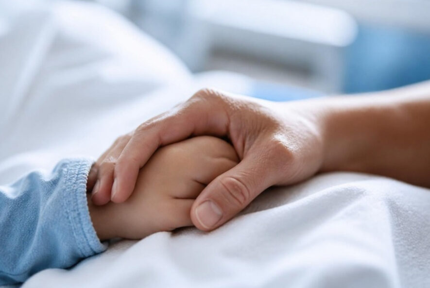 A child’s hand held by an adult’s hand on a hospital bed